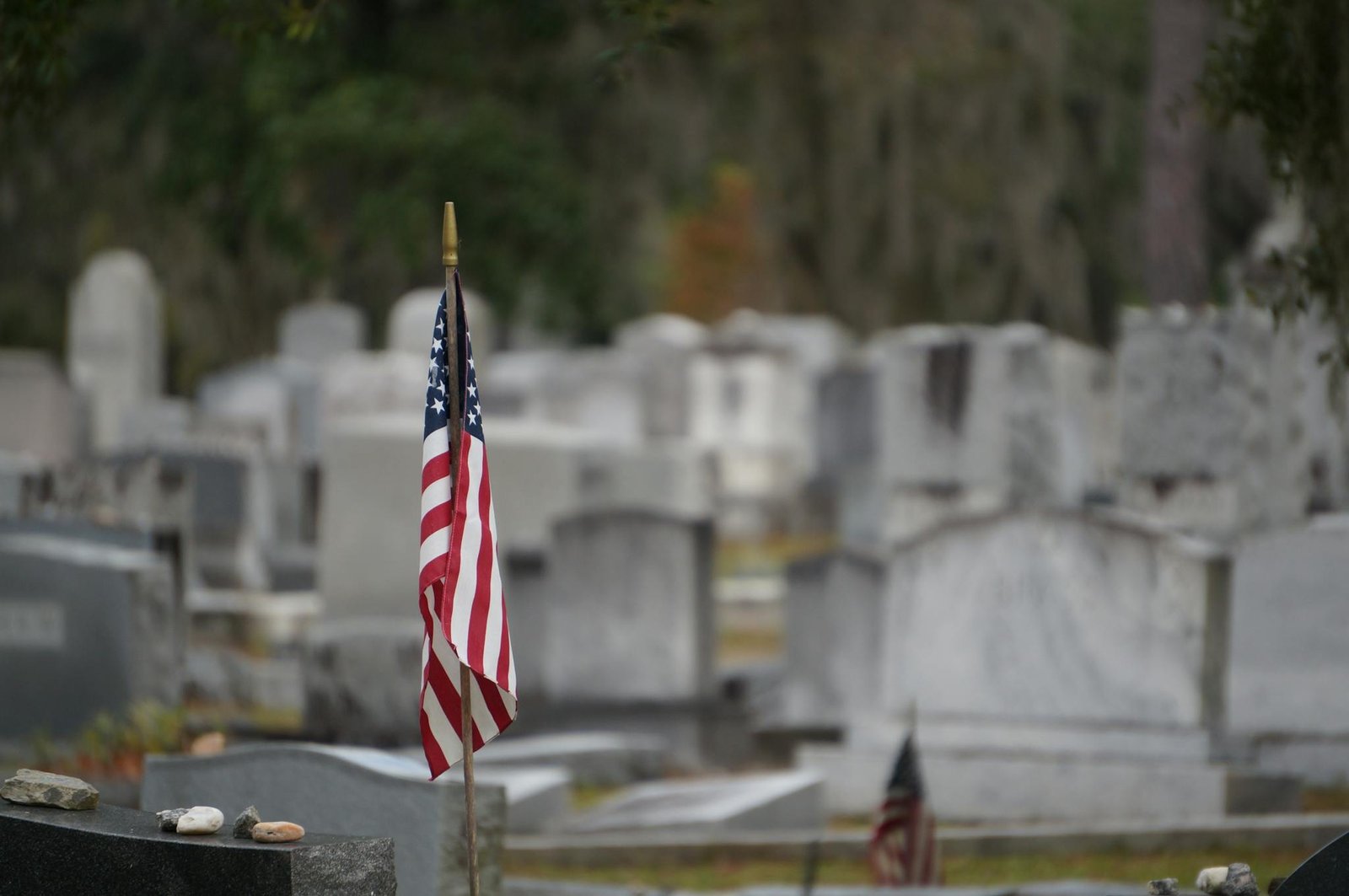 A solemn scene of gravestones with an American flag at a Savannah cemetery.