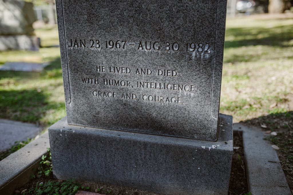 A stone tombstone with an engraved epitaph in a sunlit cemetery setting.