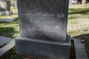 A stone tombstone with an engraved epitaph in a sunlit cemetery setting.