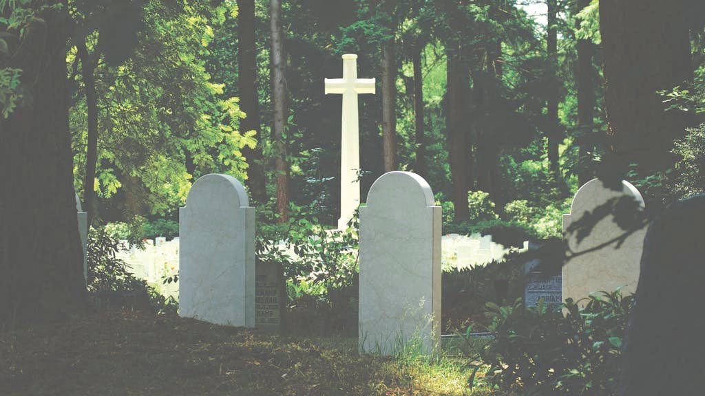 Peaceful cemetery scene with gravestones and cross amidst lush trees, evoking a sense of tranquility and reflection. Headstone cleaning services pricing.