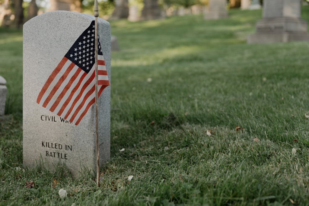 A gravestone with an American flag in a cemetery, honoring a civil war veteran. Which way do headstones face.