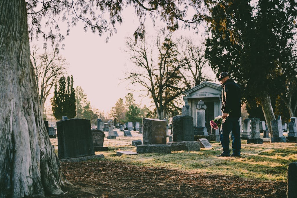 A person stands in a peaceful cemetery holding flowers in remembrance. Rules for visiting cemeteries.