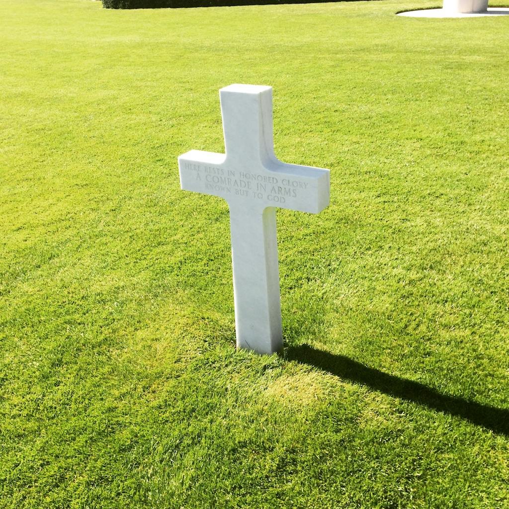 A solitary marble headstone cross in a Luxembourg cemetery under the summer sun, symbolizing remembrance.