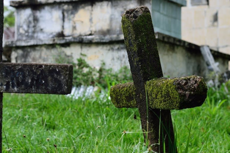 A moss-covered cross stands in an overgrown, ancient cemetery, evoking a mysterious atmosphere. How deep are graves.