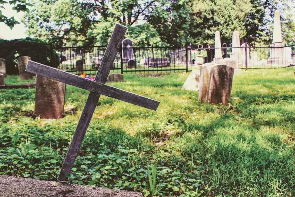 A serene cemetery with a wooden cross and tombstones on a sunny day, surrounded by nature. Can you be buried without a casket.