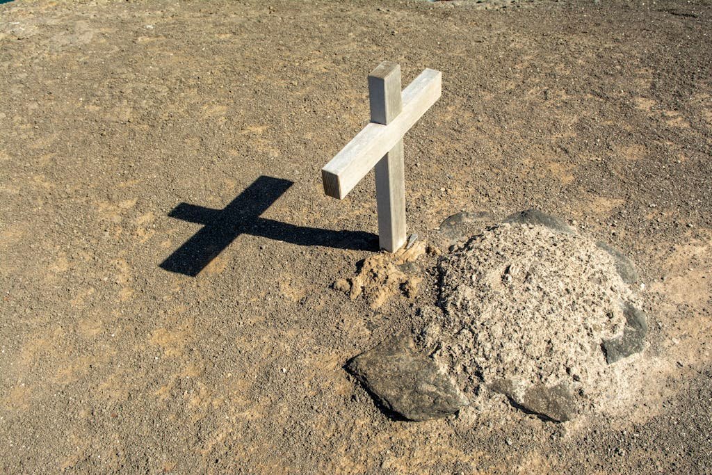 A solitary wooden cross casting a shadow on an arid grave site, symbolizing solitude and spirituality. Green burial.