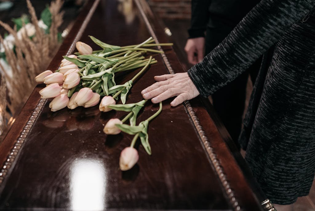A somber funeral scene with tulips placed on a wooden coffin, symbolizing loss and remembrance. Funeral planning.