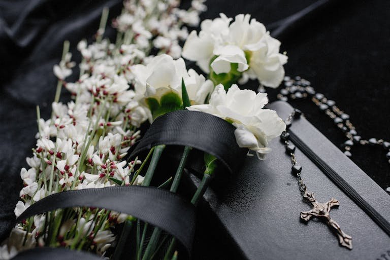 Close-up of white flowers and rosary on dark cloth, symbolizing mourning and spirituality. How long after death is the funeral.