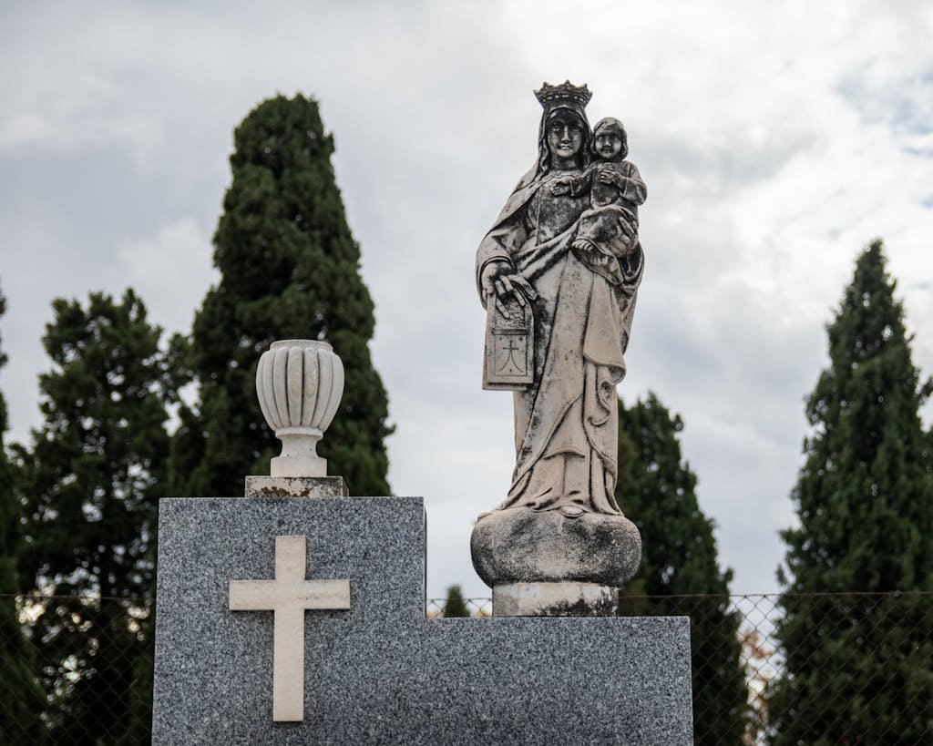 Statue of Virgin Mary and Child in a Madrid cemetery surrounded by trees.